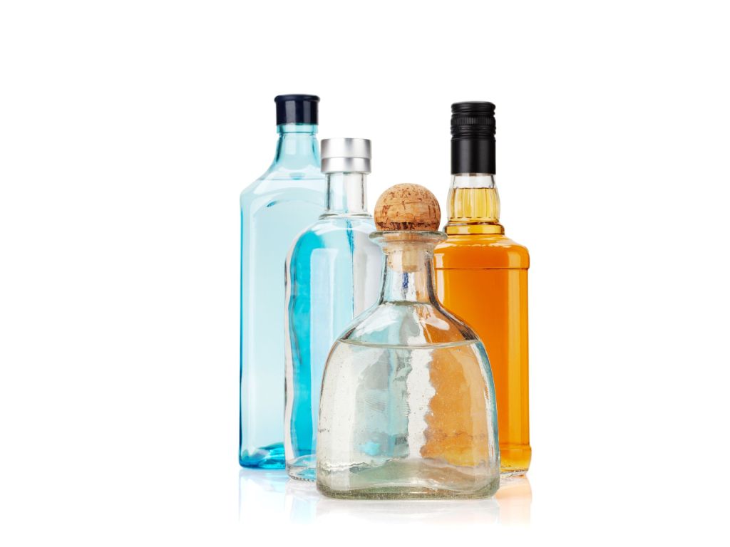 An assortment of liquor bottles and filled cocktail glasses displaying amber, golden, and clear spirits against a white background.