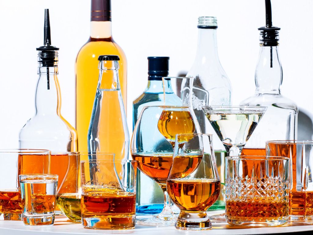 Five different spirit bottles (gin, vodka, tequila, whiskey) arranged in a cluster against a white background.