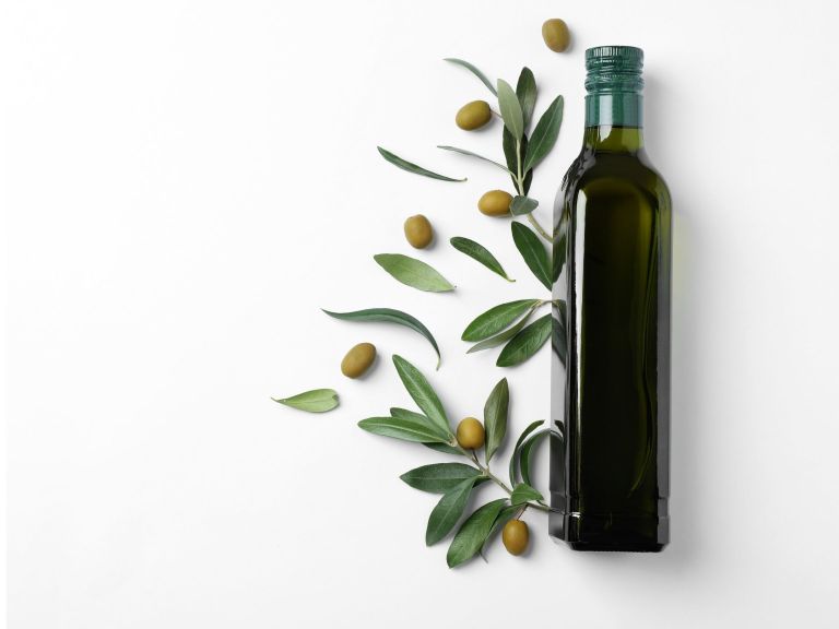A dark green glass bottle of extra virgin olive oil surrounded by fresh green olives and olive leaves on a white background.