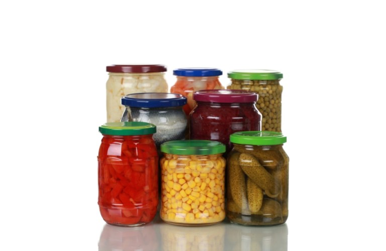 Group of glass canning jars with colorful lids, filled with homemade pickled vegetables like peppers, corn, beets, and cucumbers.