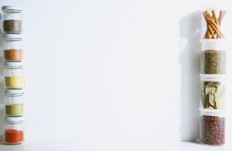 Two stacks of clear glass jars containing colorful spices and herbs, including peppercorns, paprika, cinnamon sticks, and dried leaves.