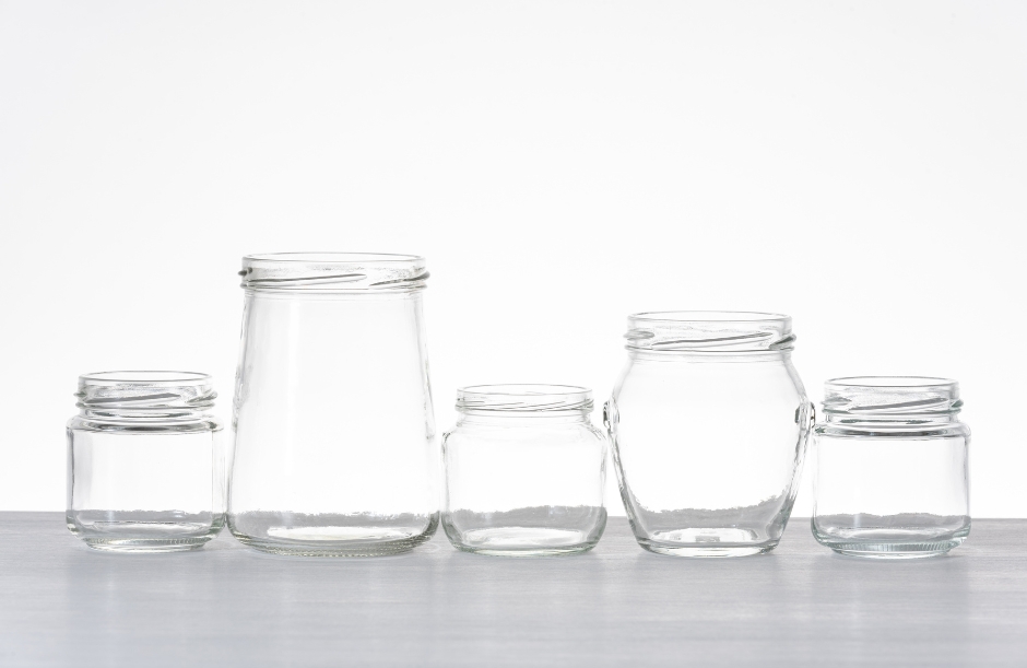 Five empty clear glass jars of varying shapes and sizes arranged neatly on a white studio background.