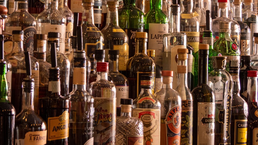 Rak bar yang penuh sesak memajang berbagai macam botol minuman keras berwarna-warni termasuk scotch, gin, tequila, rum, minuman beralkohol manis, dan banyak lagi.