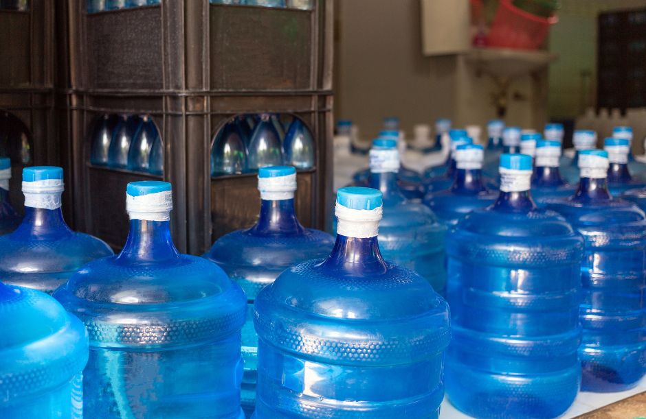 Multiple large blue 5-gallon water jugs with blue caps arranged in rows and stacked in crates, ready for delivery or office use