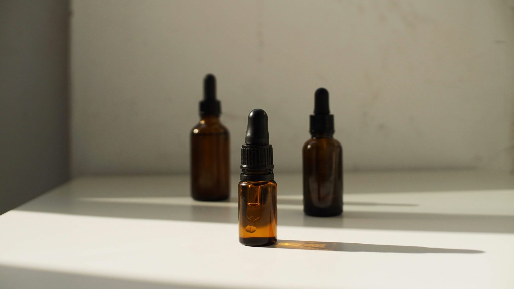 Three amber glass dropper bottles with black pipettes standing on a white surface under sharp sunlight