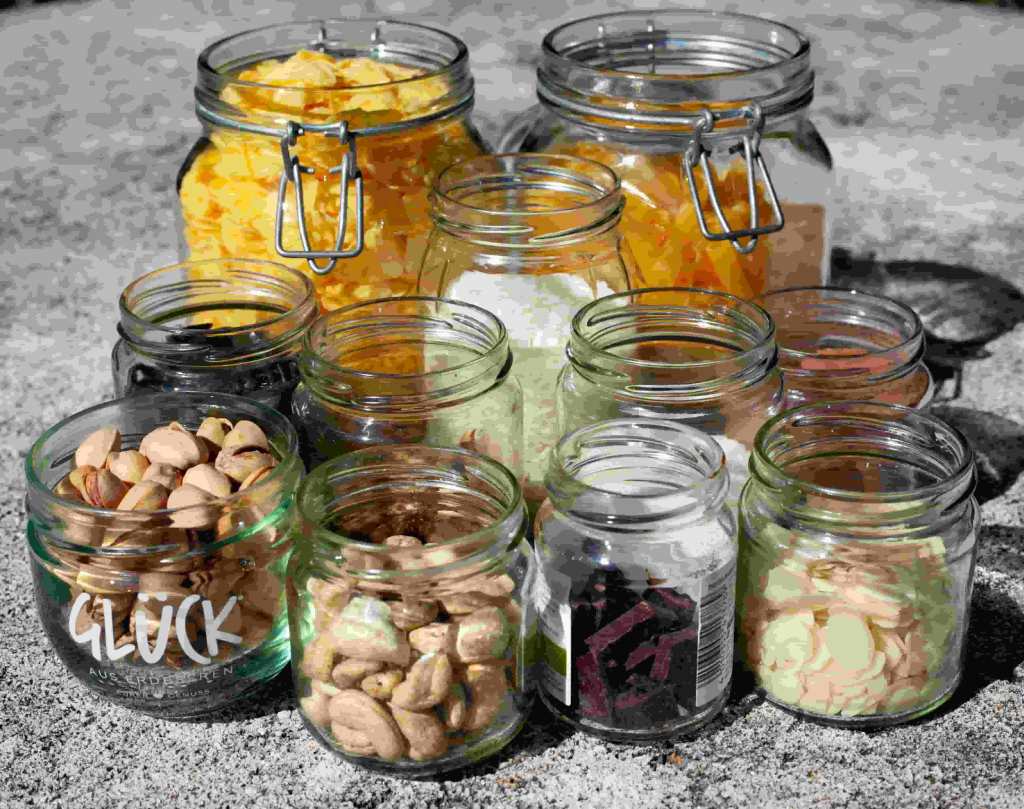 A row of various canning jar sizes and wholesale food storage containers filled with dry baking ingredients on a kitchen countertop.