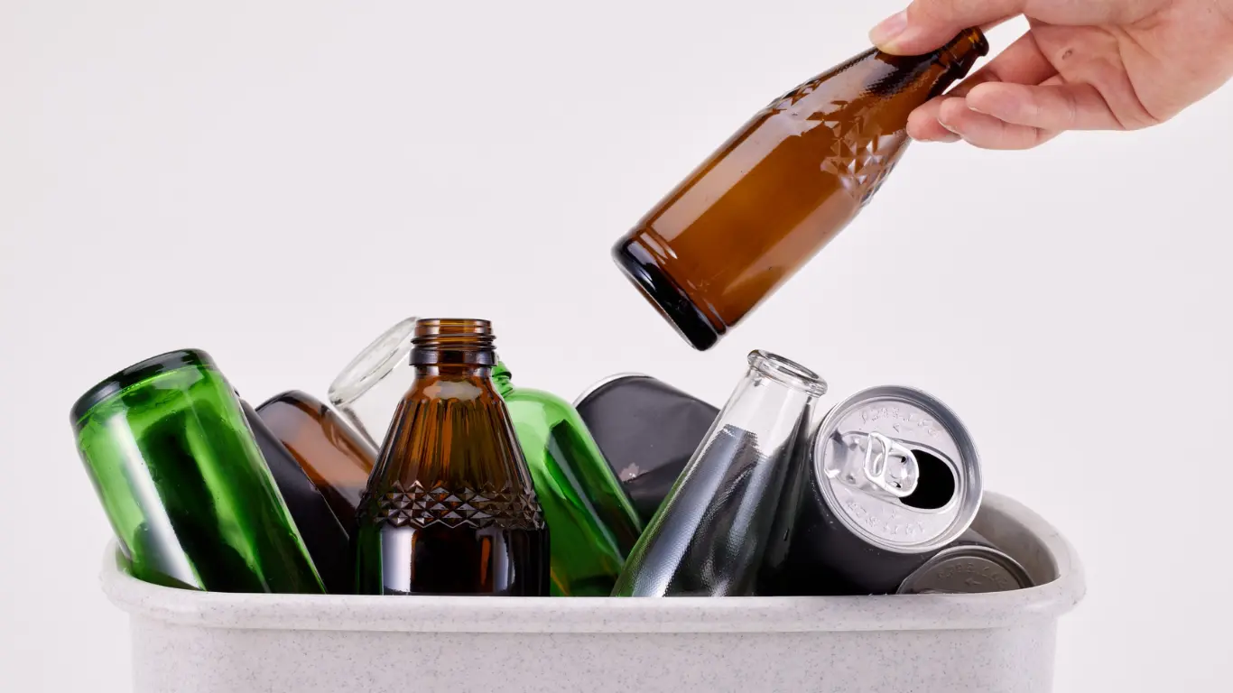 Placing an amber glass bottle into a white recycling bin filled with sustainable bulk glass packaging supplies.