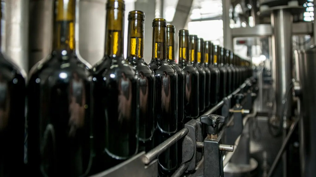 Automated industrial bottling line transporting bulk bordeaux wine containers inside a commercial manufacturing plant.