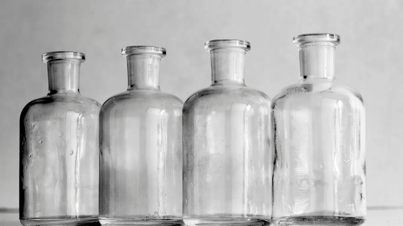 Four clear glass flat shoulder bottles lined up against a light neutral background