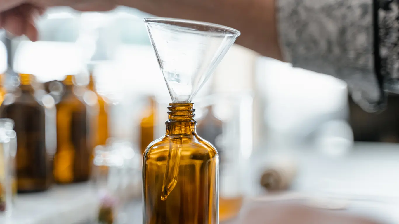 Clear glass funnel placed inside the narrow neck of an amber glass Boston round bottle