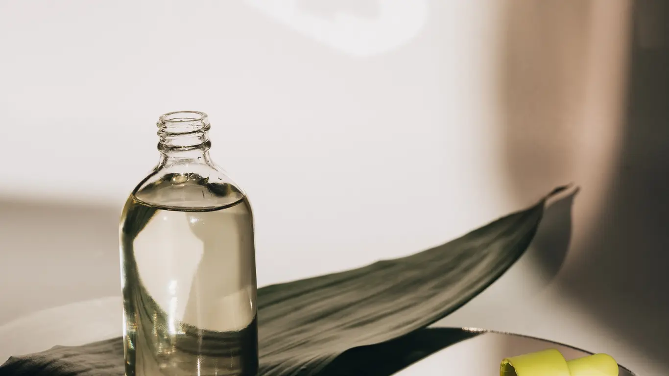 Clear glass Boston round bottle filled with pure liquid resting on a dark green leaf